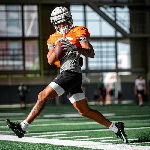 Football player in orange jersey running with ball on indoor turf field