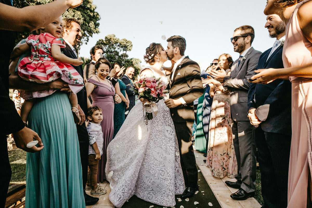 Bride and groom kissing at outdoor wedding, guests celebrating with flower petals